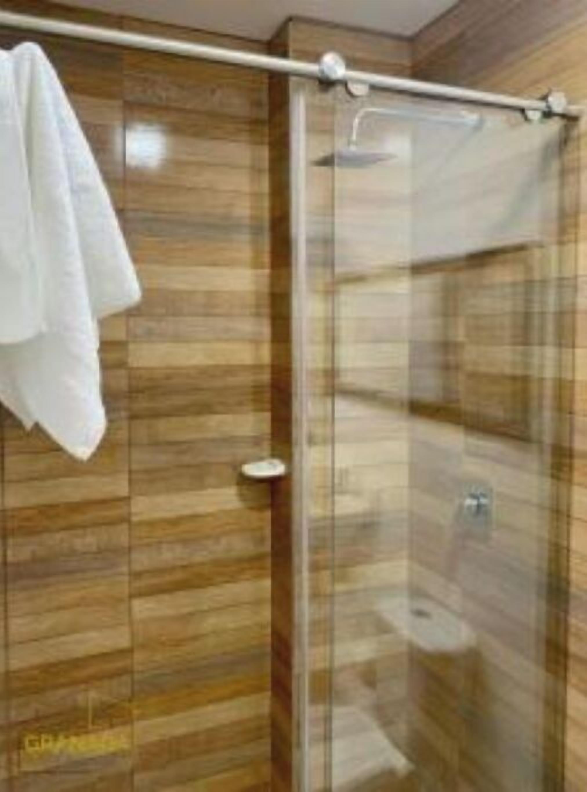A modern bathroom with a glass shower enclosure, wooden paneling, and a towel hanging on the wall.