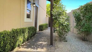 Uma trilha leva a uma casa com varanda coberta, um pequeno jardim e um caminho de acesso de cascalho.