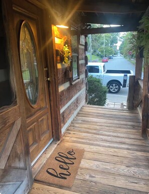 Fachada de madera con puerta de vidrio, felpudo y un vehículo estacionado afuera.
