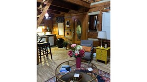 A cozy room with a wooden ceiling, a round coffee table with a vase of flowers, a sofa with a cushion, and a yellow side table. - Log Cabin on Main St. In the ❤️ of Winston Salem. Sleeps 4 comfortably.  (Winston-Salem)