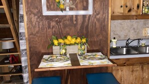A wooden kitchen with a dining table set for two, a window with a lemon wreath, and a sink. - Log Cabin on Main St. In the ❤️ of Winston Salem. Sleeps 4 comfortably.  (Winston-Salem)