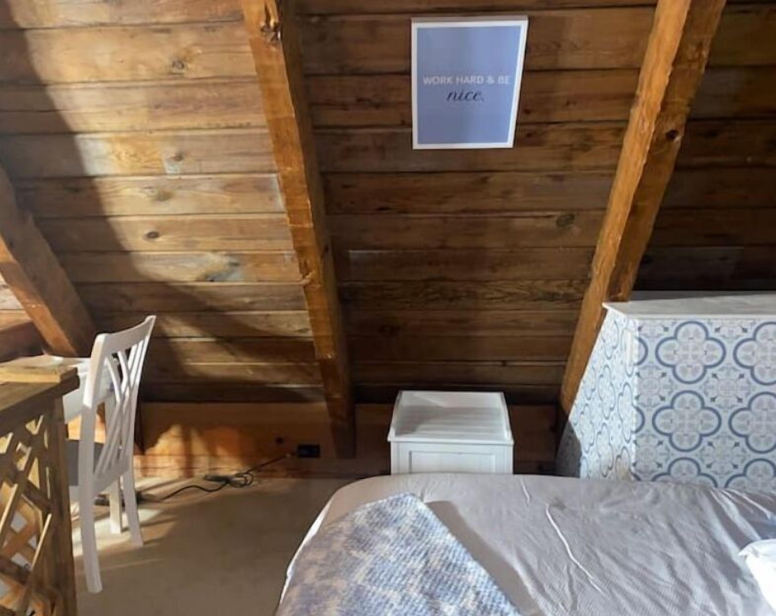 A wooden cabin room with a bed, a small white table, and a chair.