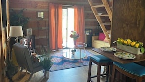 A rustic cabin interior with a loft bed, a dining area with a table and chairs, and a cozy seating area with a sofa and a lamp. - Log Cabin on Main St. In the ❤️ of Winston Salem. Sleeps 4 comfortably.  (Winston-Salem)
