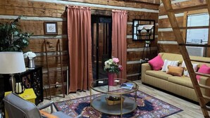 A cozy log cabin interior with a sofa, armchair, and a round coffee table with a vase of flowers. - Log Cabin on Main St. In the ❤️ of Winston Salem. Sleeps 4 comfortably.  (Winston-Salem)