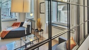 A modern living room with a glass partition, a sofa set, a coffee table, and a view of a cityscape through large windows.