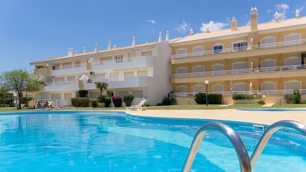 A swimming pool with a clear blue water surface, surrounded by a white building with balconies and a flat roof. - Finfoot Black Apartment, Vilamoura, Algarve (Quarteira)