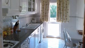 A kitchen with white cabinets, a granite countertop, a sink, and a window with curtains. - Finfoot Black Apartment, Vilamoura, Algarve (Quarteira)