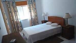 A bedroom with a bed, two bedside lamps, a nightstand, a wooden dresser, and a small table with a lamp. - Finfoot Black Apartment, Vilamoura, Algarve (Quarteira)