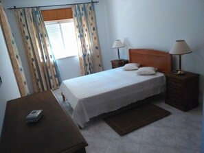 Un dormitorio con una cama, dos lámparas de noche, una mesita de noche, un aparador de madera y una pequeña mesa con lámpara.