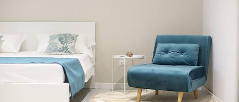 Un dormitorio con una cama, un sillón azul, una mesita auxiliar y un tapete redondo.