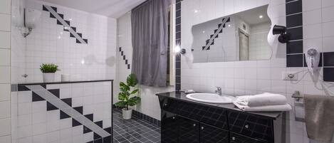 Une salle de bain moderne avec des carreaux noirs et blancs, un meuble-lavabo noir, un miroir, un évier et une plante en pot.