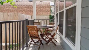 Una veranda coperta con tavolo e sedie, una recinzione in legno e vista sugli edifici vicini.