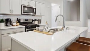 Una cucina moderna con mobili bianchi, un forno a microonde in acciaio inox, un lavello e un'isola in legno con un vassoio.