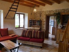 A cozy living room with a red sofa, a wicker sofa, a wooden table, and a ladder against the wall. - Old freestone farm built in 1880 in the middle of Alsace and nature (Fouchy)