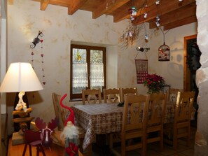 A dining area with a table set for four, wooden chairs, a lamp, a decorative gnome, and a window with lace curtains. - Old freestone farm built in 1880 in the middle of Alsace and nature (Fouchy)