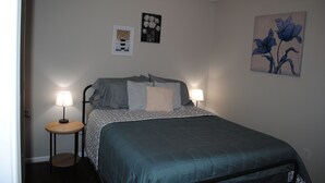 Een slaapkamer met een bed, twee bedlampen, een klein rond tafeltje en twee foto’s aan de muur.