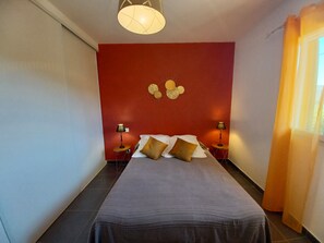 A bedroom with a large bed, two bedside tables with lamps, a red accent wall, and a ceiling light fixture.