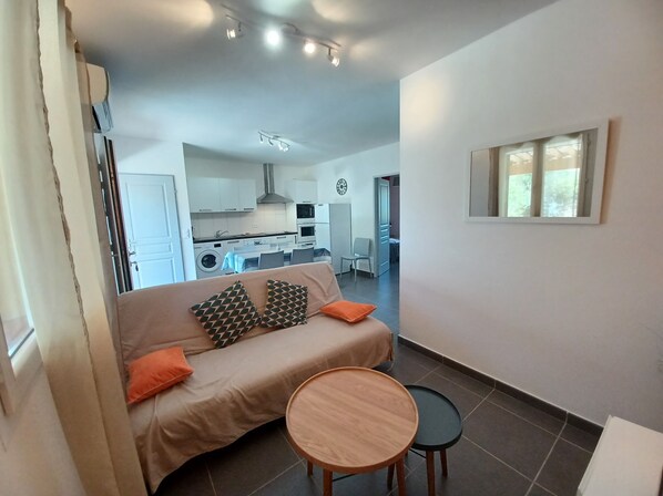 A modern living room with a sofa, two round tables, and a kitchen in the background.