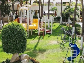 Guests can enjoy a fun-filled day at our outdoor play area, featuring a slide and swing set amidst lush greenery and a beautifully manicured lawn.