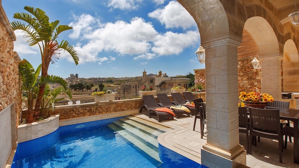 Una piscina en la azotea con sillas de descanso y un muro de piedra.