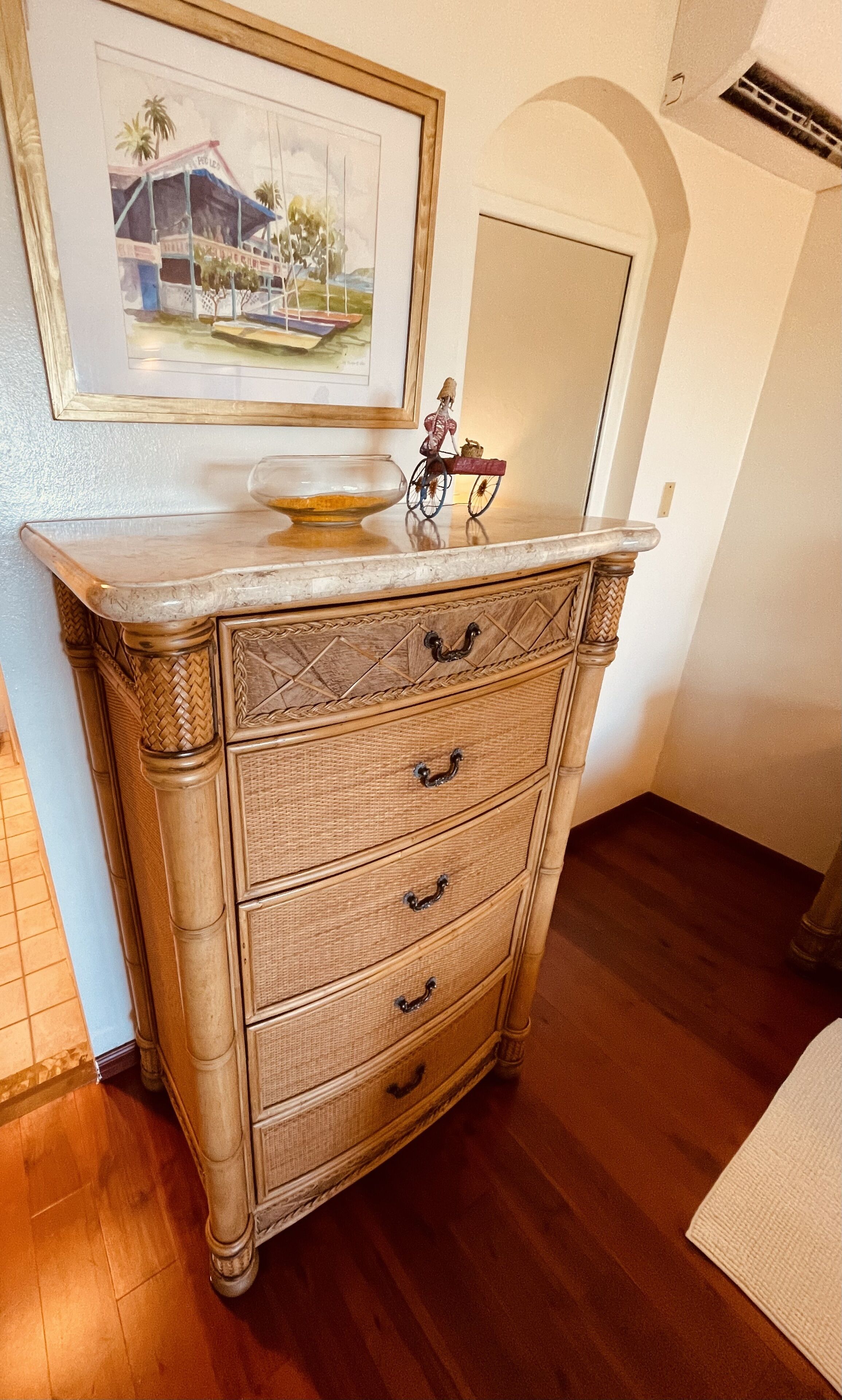 A wooden dresser with drawers and a mirror, a framed painting above it, and a small figurine on top.