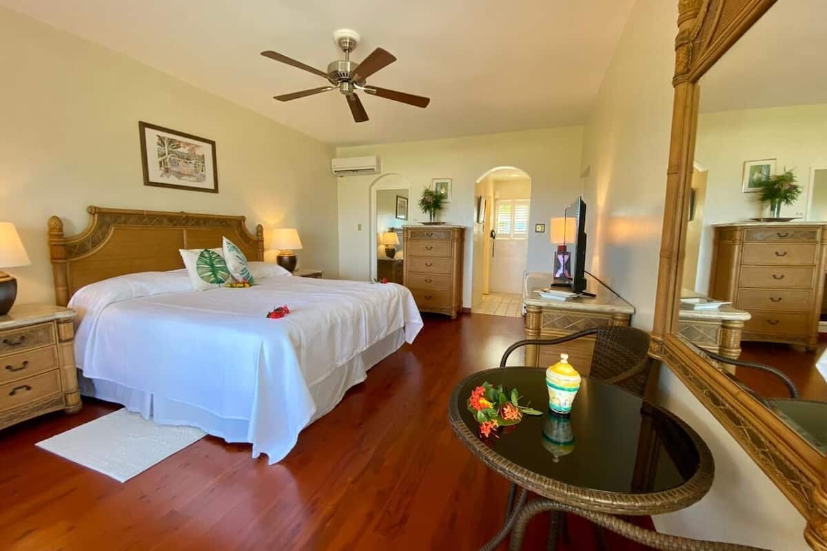 A hotel room with a bed, a dining table with chairs, a ceiling fan, a mirror, and a dresser.