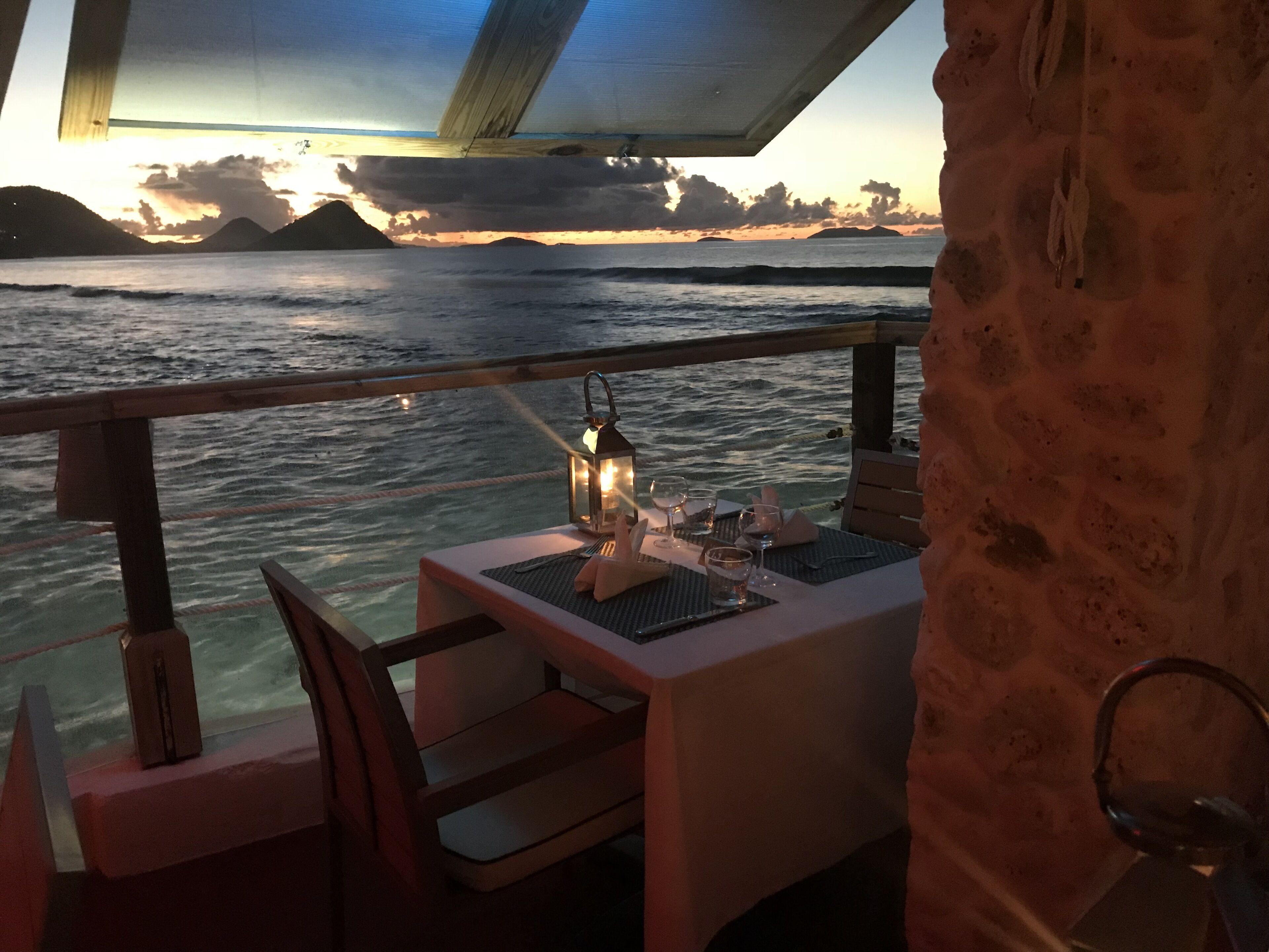 A table set for two with a view of the ocean and a sunset.