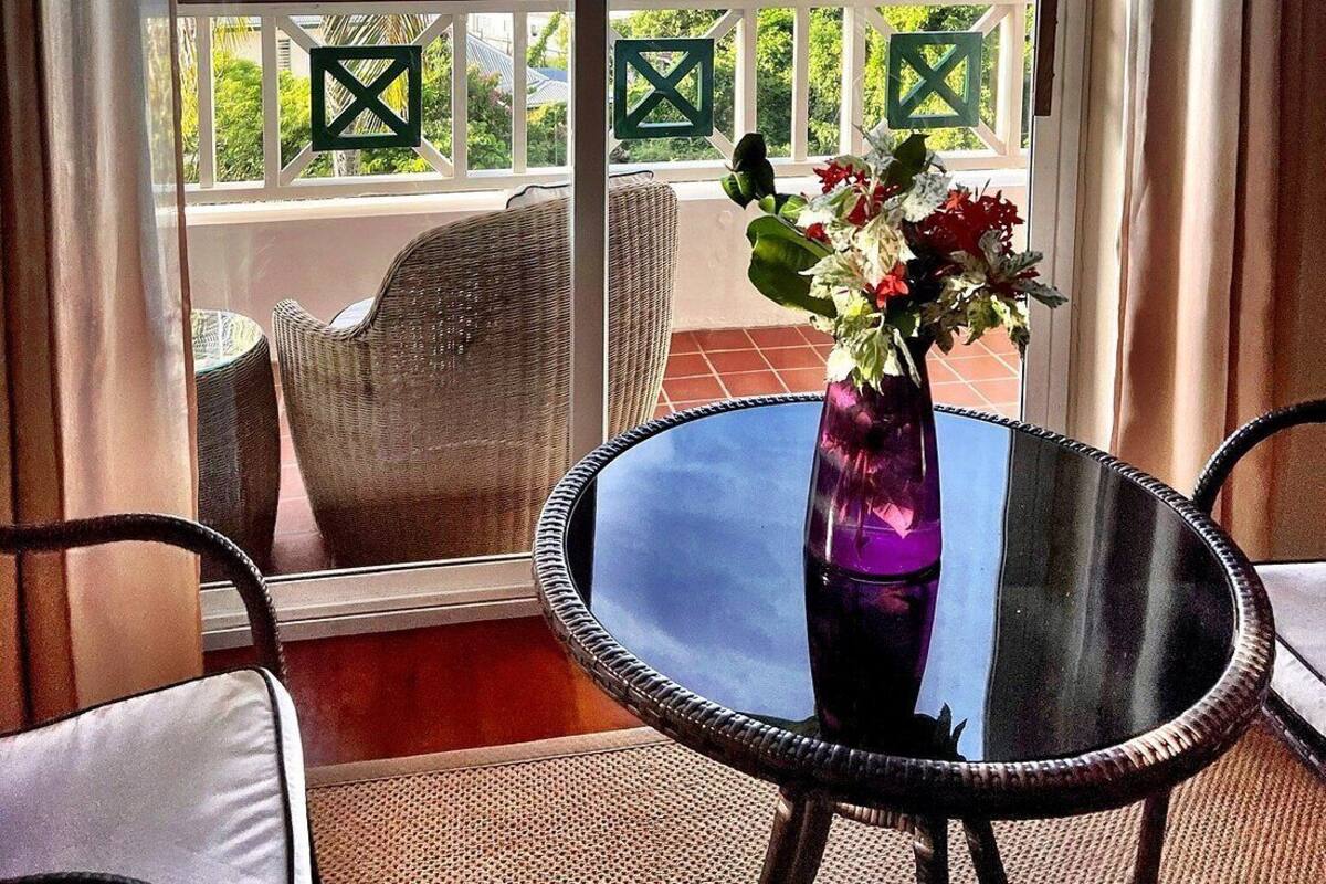 A balcony with a view of the ocean, wicker furniture, and a glass table with a vase of flowers.
