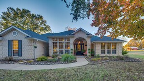A two-story house with a brick exterior, a front entrance with a door, and a small garden area with plants and a pathway leading to the entrance. - 'The Crown Goose' - Bullard Home w/ Pool & Spa! (Bullard)