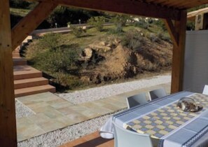 Eine Terrasse im Freien mit Tisch und Stühlen, ein Steinweg und ein Blick auf einen angelegten Garten mit Stufen, die einen Hügel hinaufführen.