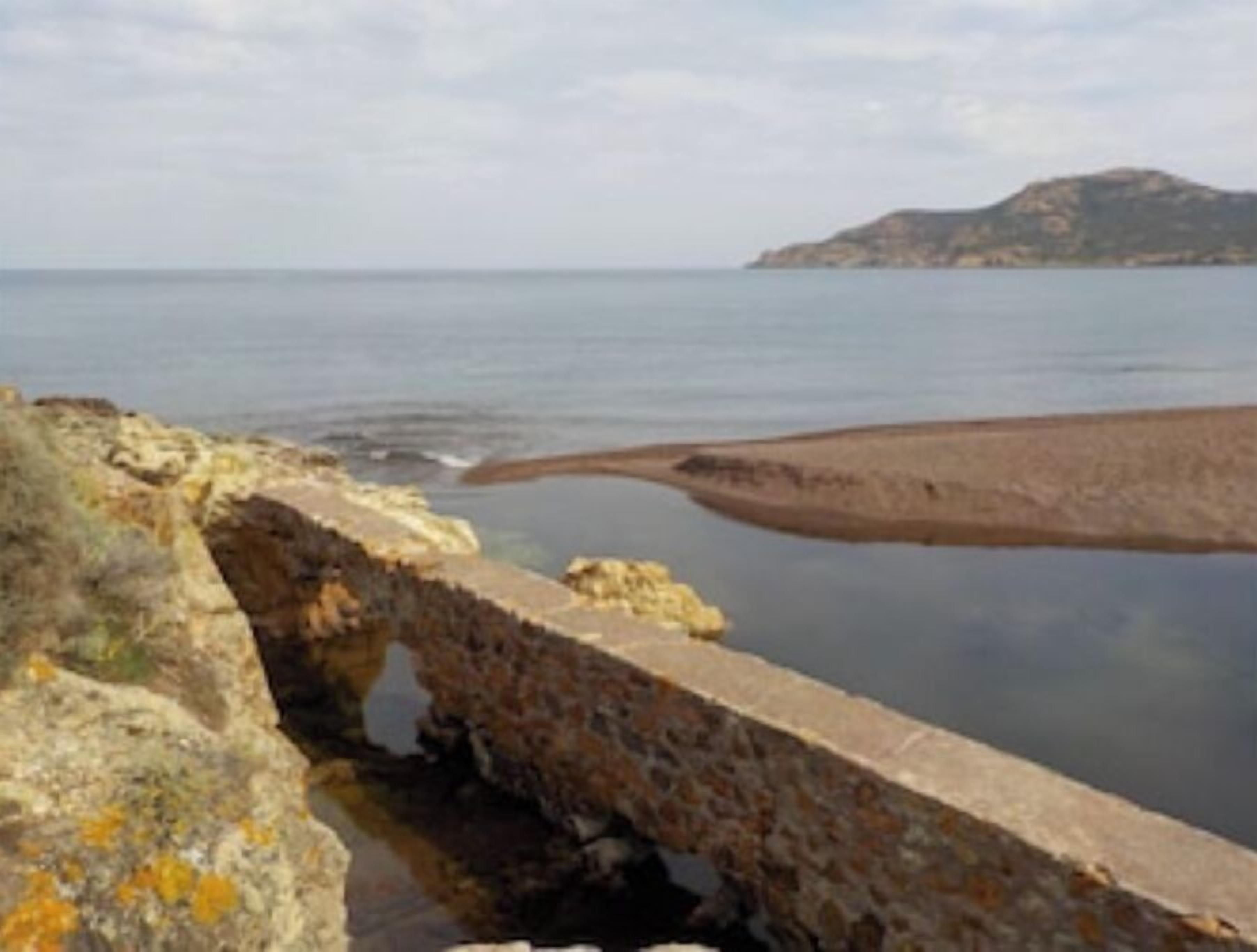 A coastal stone structure with a view of the sea and a distant hill.