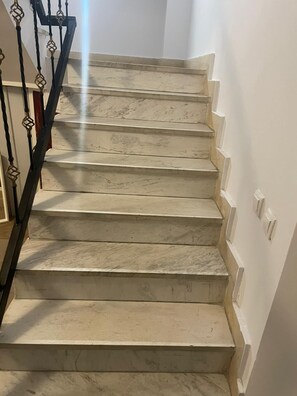 Una escalera de mármol con barandilla de metal negro y paredes blancas.