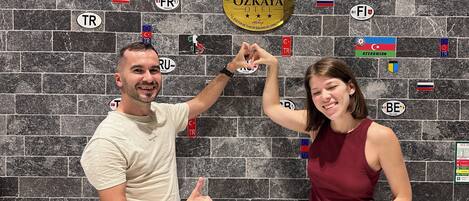A man and a woman posing in front of a wall with various national flags and a sign that reads 'ÖZKAYA HOTEL'.