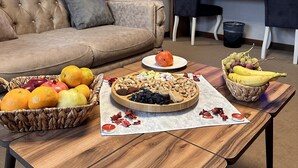 A living room with a sofa, two chairs, a wooden coffee table with fruit and a plate, a television, and a door with a heart-shaped decoration. - Ozkaya Otel (Sivas)