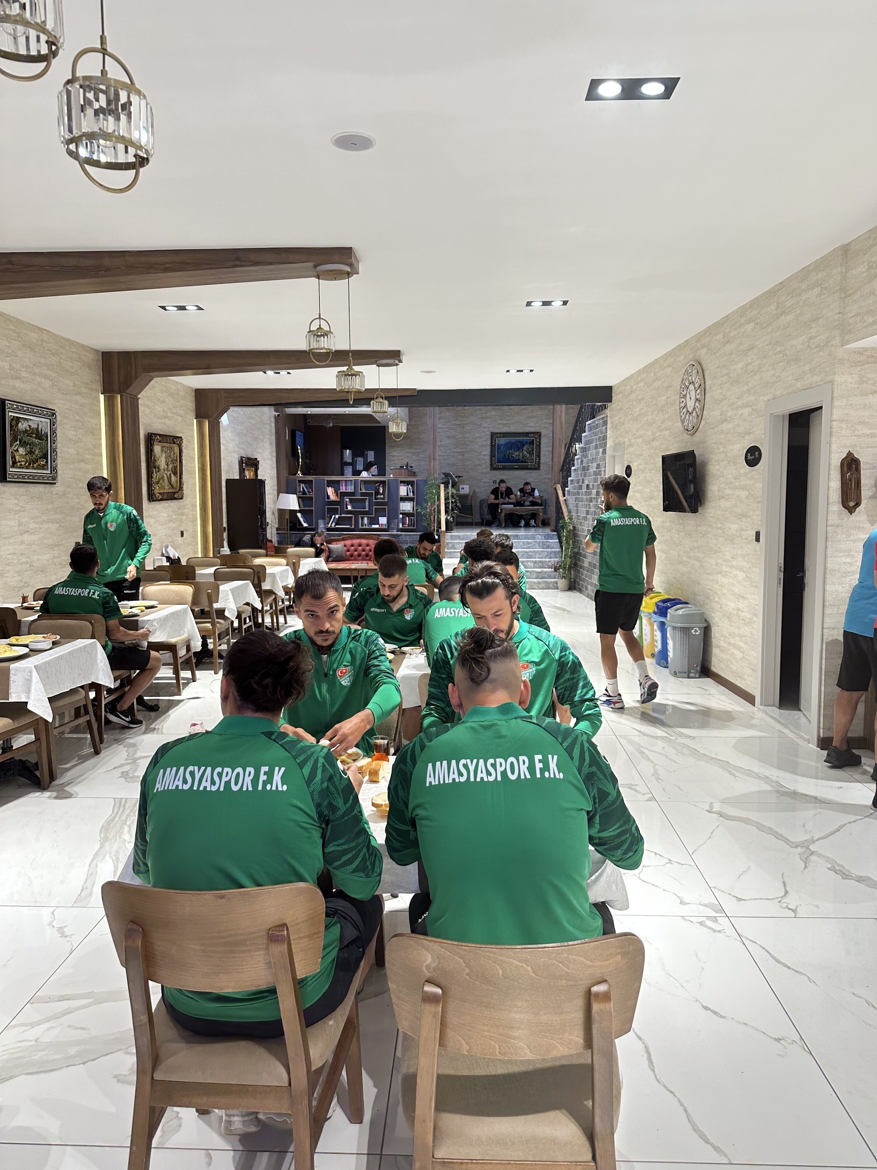 A group of people in green jackets sitting at a table in a well-lit dining area with a high ceiling and modern decor.