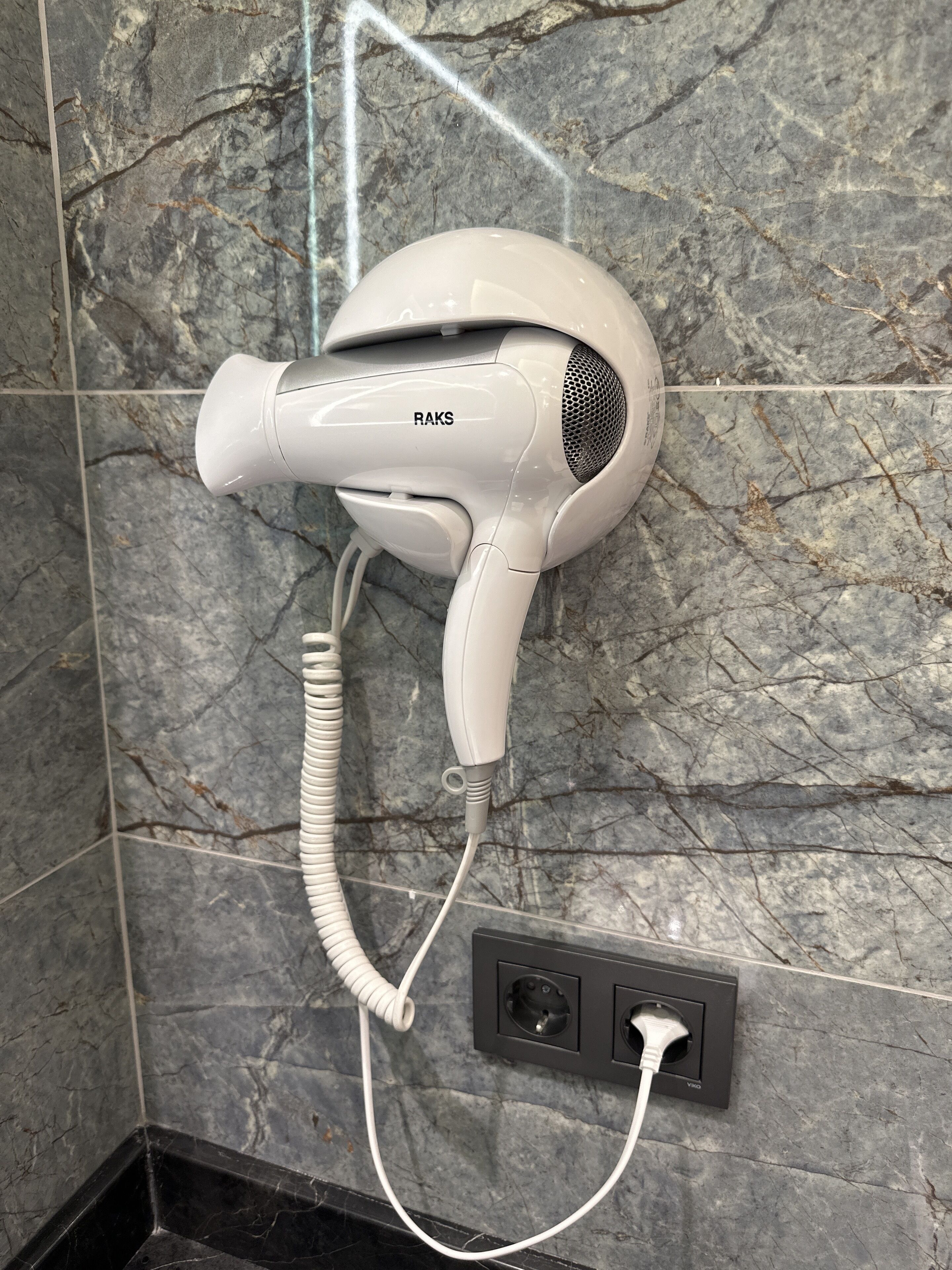 A hair dryer mounted on a wall with a marble pattern, connected to a power outlet.