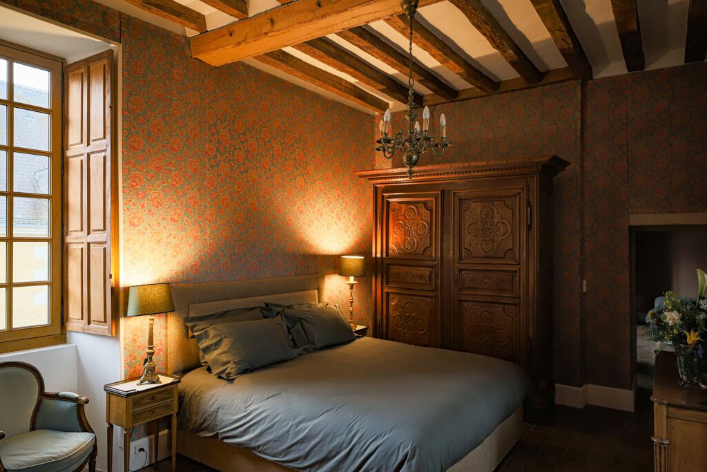Een slaapkamer met een groot bed, een houten hoofdbord, twee nachtkastjes met lampen, een stoel en een raam met gordijnen.