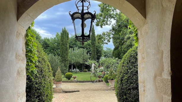 Ein bogenförmiger Steinweg führt zu einem Garten mit einer hängenden Laterne.
