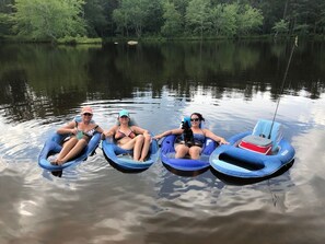 Three people floating on blue inflatable tubes in a calm lake surrounded by trees.