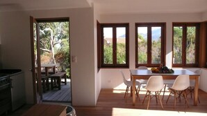 A modern kitchen with a dining area. There is a wooden table with chairs and a view of the outdoors through large windows. - New eco-certified house near the beach (Galéria)