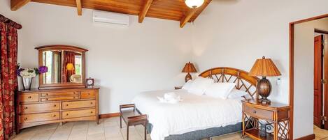 A bedroom with a wooden ceiling, a bed with white bedding, a wooden dresser, a mirror, two bedside lamps, and a small table with a lamp.