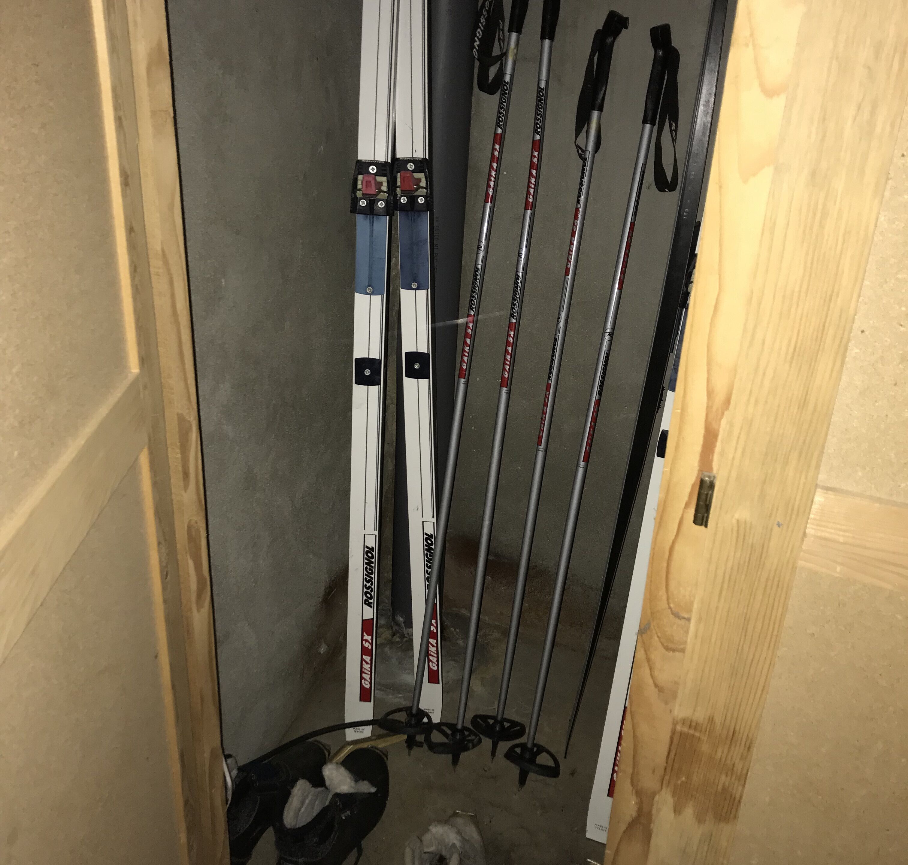 A corner of a room with a wooden door, a pair of skis leaning against the wall, and a pair of ski poles.