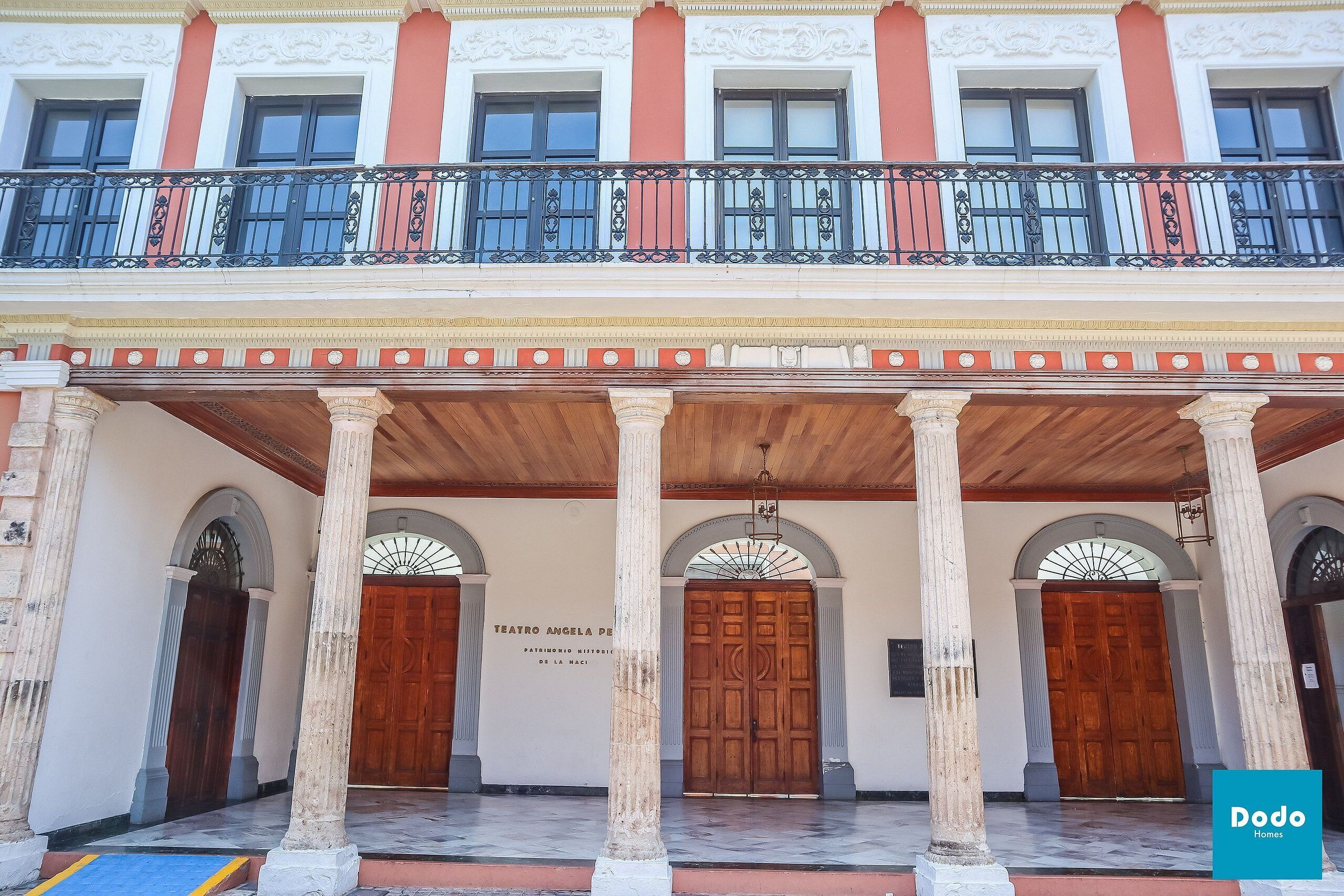 Un edificio con vestíbulo cubierto, columnas y un balcón con barandilla decorativa.