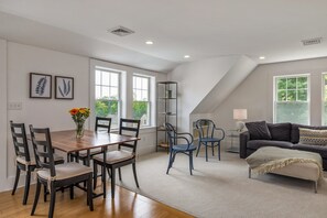 A spacious living area with a dining table, chairs, a sofa, and a tall shelving unit.