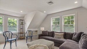 Una sala de estar moderna con un sofá seccional gris, un sillón azul, un reposapiés blanco y un estante negro.