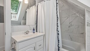 Un baño moderno con un tocador blanco, una bañera y una cortina de ducha con flecos.