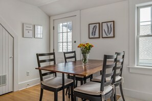 Un coin repas avec une table en bois et six chaises, un vase rempli de fleurs et des œuvres d’art encadrées accrochées au mur.