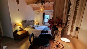 Une chambre confortable avec un plafond en bois, un lit recouvert de linge de maison blanc, une table de chevet avec une lampe et une étagère murale ornée d’objets décoratifs.