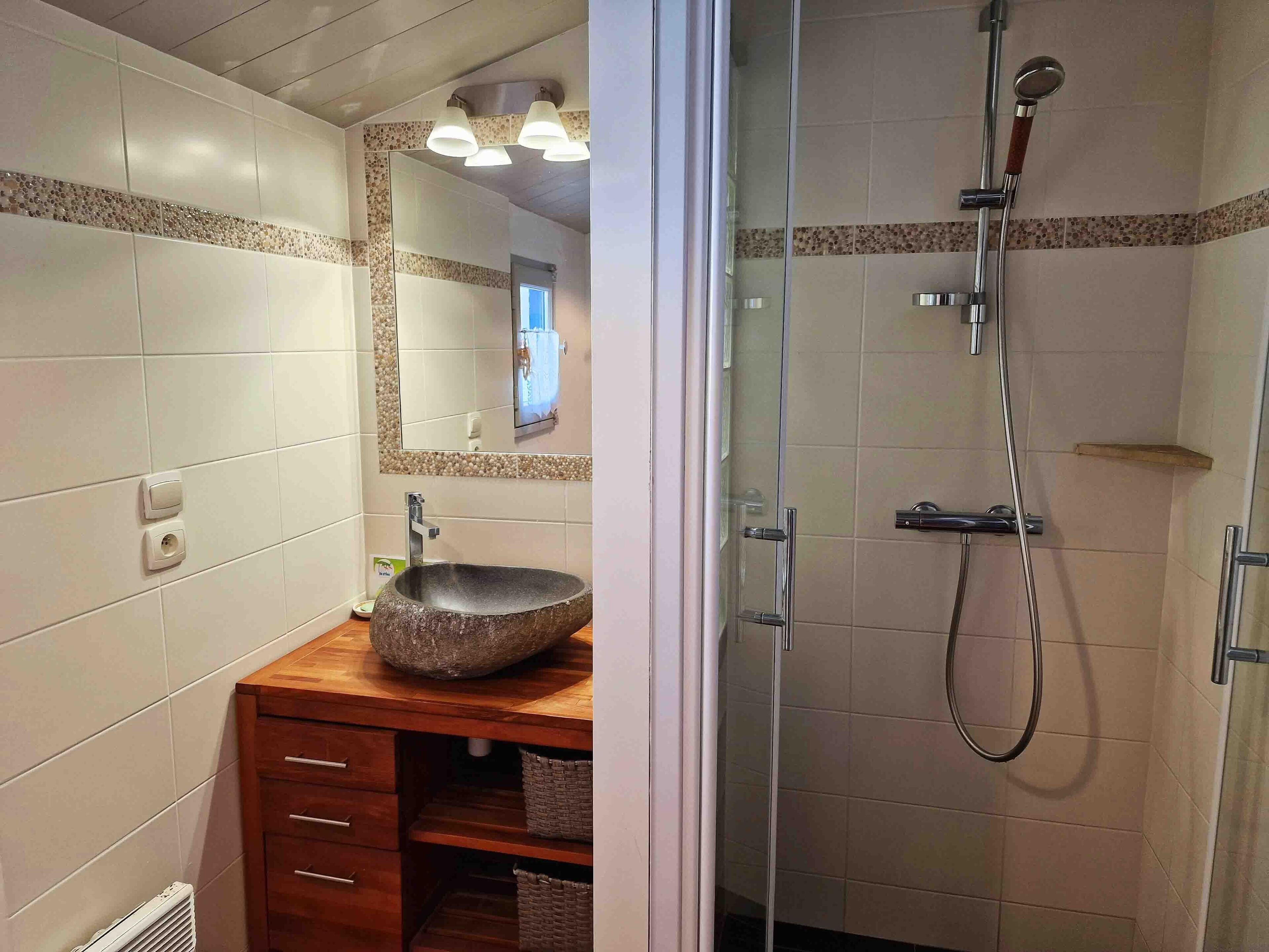 Une salle de bain moderne avec un lavabo en pierre, un meuble-lavabo en bois et une douche séparée par des parois en verre.
