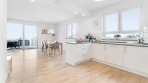 A modern kitchen with white cabinets, a wooden dining table, and a large window.